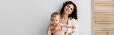 Gülümseyen anne, bebeği kucağında katlanan ekranın yanında, pankartta 