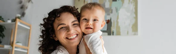 stock image happy and curly woman holding in arms baby daughter in romper, banner