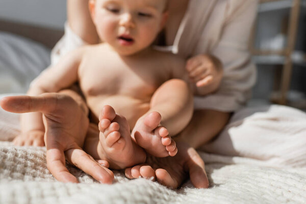 mother holding in hands tiny bare feet of baby daughter in bedroom 