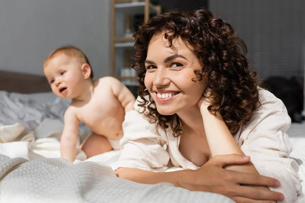 Happy Mother Curly Hair Looking Camera Blurred Baby Girl Bed — Stock Photo, Image