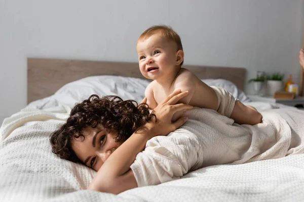 ベッドルームの母親の後ろに寝そべっている元気な赤ちゃん — ストック写真
