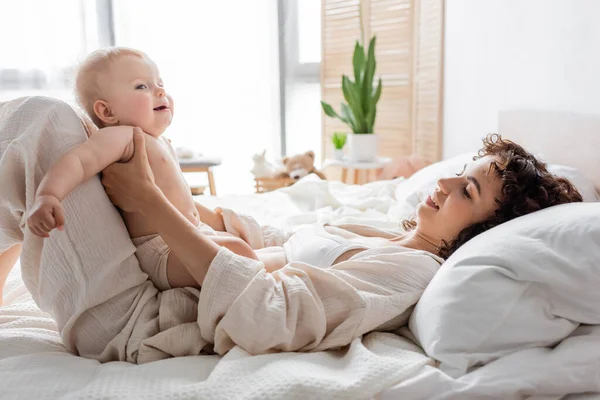 幸せな女性ですラウンジウェアでベッドの上に横たわっていますかわいいです赤ちゃん娘 — ストック写真