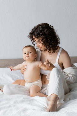 Pijamalı kıvırcık anne, sabahları yatakta küçük kızına bakıyor. 