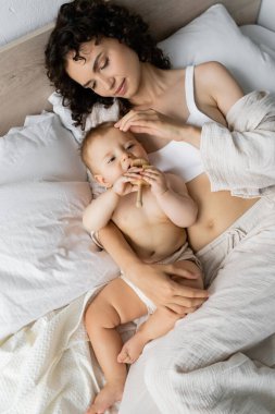 Pijamalı esmer bir annenin bebeğe dokunuşunu yatakta oyuncağıyla 