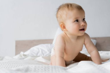 İç çamaşırlı küçük bir çocuk evde beyaz bir yatakta oturuyor. 