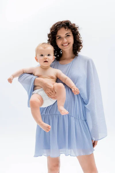 Χαρούμενη Γυναίκα Φόρεμα Κρατώντας Μωρό Και Κοιτάζοντας Κάμερα Απομονωμένη Λευκό — Φωτογραφία Αρχείου