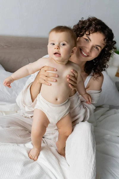 Ευτυχισμένη Γυναίκα Που Κρατά Μωρό Εσώρουχα Στο Κρεβάτι Στο Σπίτι — Φωτογραφία Αρχείου