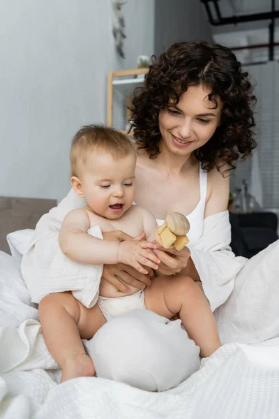 Curly Mother Holding Toy Infant Daughter Bed — Stock Photo, Image