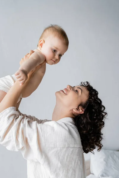 Curly Woman Smiling While Lifting Baby Girl Bedroom Morning — Stock Photo, Image