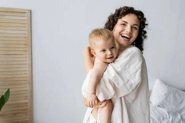 Mujer Feliz Mirando Cámara Mientras Abraza Hija Dormitorio — Foto de Stock