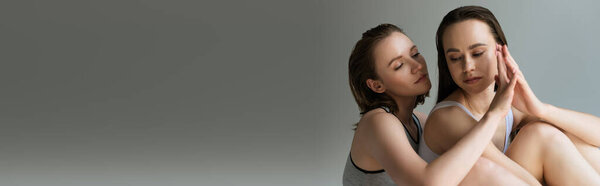 чувственные лесбиянки в нижнем белье взялись за руки, сидя изолированно на сером баннере