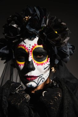 Çelenk takmış kadın portresi ve siyah arka plandaki kameraya bakan Catrina makyajı. 