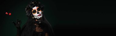 Meksikalı Santa Muerte kostümlü bir kadın koyu yeşil arka planda zar atıyor. 