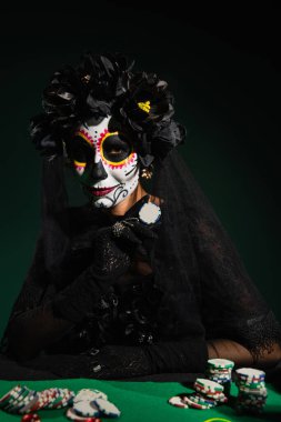 Santa Muerte cadılar bayramı kostümlü bir kadın elinde koyu yeşil arka planda çip oynuyor. 