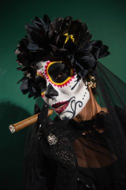 Yeşil arka planda puro tutan Santa Muerte cadılar bayramı kostümlü kadın portresi 