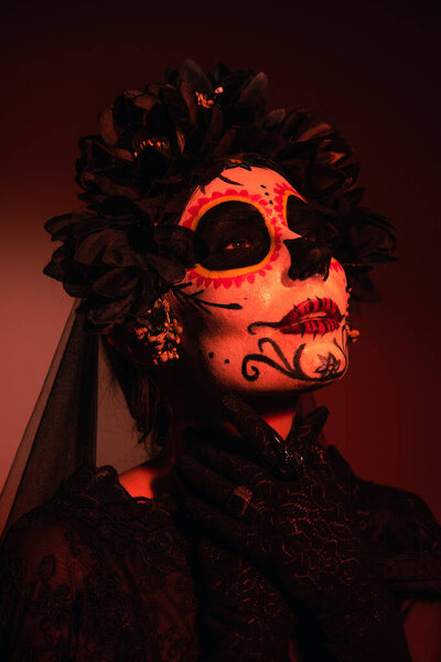 Portrait of woman in costume and catrina makeup on burgundy background with red lighting 