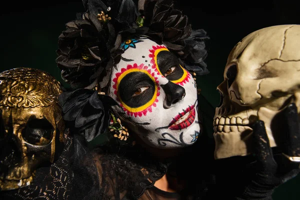 Woman in black wreath and cartina makeup holding skulls isolated on black