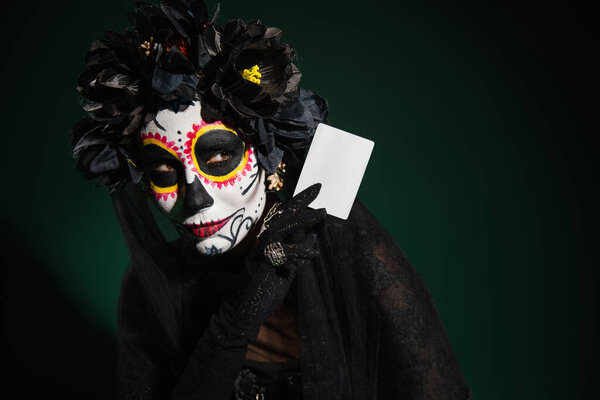 Woman in mexican santa muerte costume holding card on dark green background 