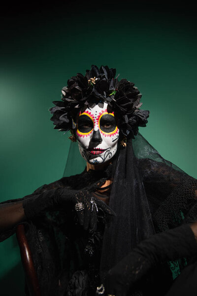 Woman in creepy day of death costume looking at camera on green background 