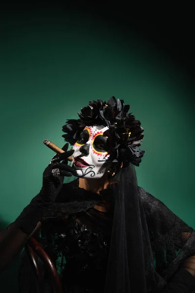 穿着死亡化妆和黑色服装的女人在绿色背景下抽雪茄 — 图库照片