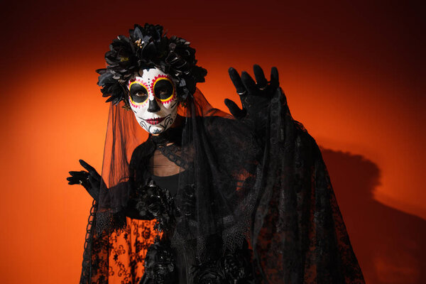 Woman in creepy santa muerte costume and wreath looking at camera on red background 
