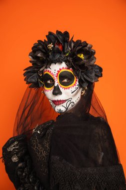 woman in traditional day of dead costume and makeup touching black veil isolated on orange clipart