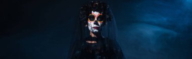 woman in mexican day of dead makeup and black wreath with veil on dark background with blue smoke, banner clipart