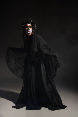 Ürkütücü Noel Baba kostümü ve koyu arkaplanda Catrina makyajı olan uzun boylu bir kadın.