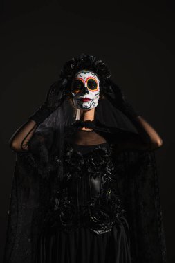 Catrina makyajlı kadın ve Santa Muerte kostümlü siyah peçeli kara çelenge dokunan kadın.