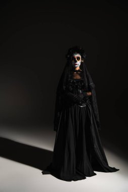full length of woman in mexican day of dead costume and spooky makeup on black background clipart