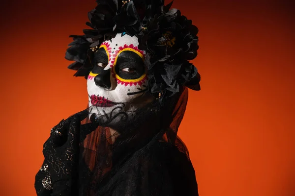 Portrait of woman with sugar skull makeup touching black veil on red background