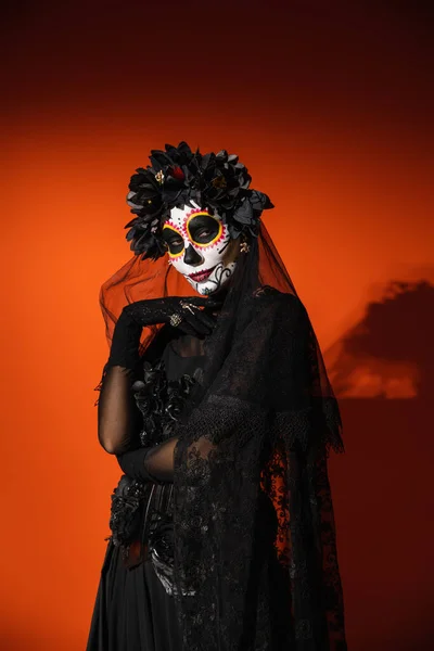 Woman in creepy mexican day of death costume and makeup looking at camera on red background