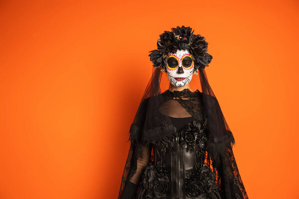 woman in witch halloween costume and spooky makeup standing with closed eyes isolated on orange