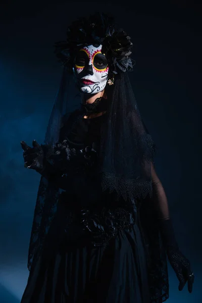 woman in santa muerte makeup and creepy costume with black lace veil on dark blue background