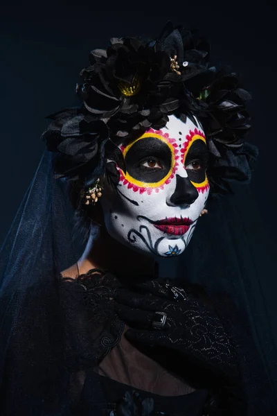 portrait of woman in black wreath and mexican catrina makeup on dark blue background