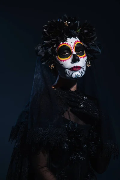 woman in creepy halloween makeup and black costume of witch on dark background