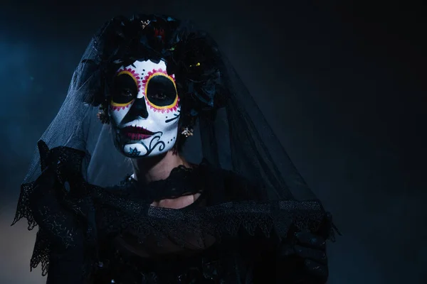 woman in spooky halloween makeup and black veil with lace on dark blue background