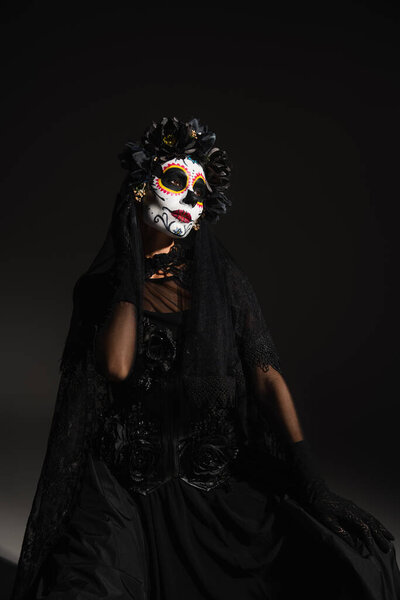 woman in creepy costume and mexican day of dead makeup sitting on black background