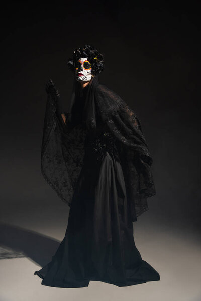 Full length of woman in traditional day of dead costume and catrina makeup posing on black background
