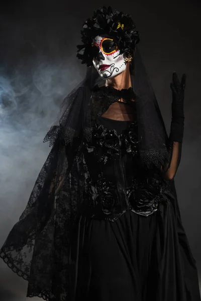 穿着黑色女巫服装的女人和在浓雾笼罩下的深色背景下化妆的令人毛骨悚然的哈露 — 图库照片