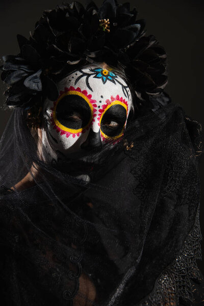 woman in traditional day of dead makeup obscuring face with dark veil isolated on black