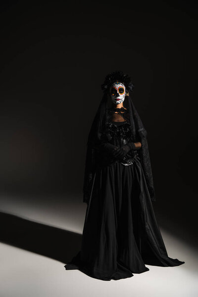 full length of woman in mexican day of dead costume and spooky makeup on black background