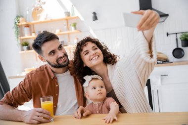 Kıvırcık kadın mutlu koca ve küçük kızıyla selfie çekiyor.