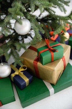 Kurdeleli renkli hediye kutularının yüksek açılı görüntüsü ve süslü noel ağacının yanında fiyonklar. 