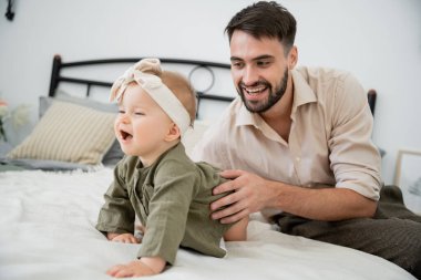 Mutlu sakallı baba yatakta emekleyen bebeğe bakıyor.