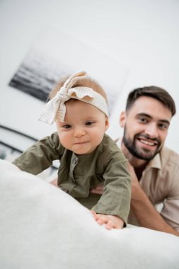 Mutlu sakallı baba, bebek yatakta sürünürken kameraya bakıyor.