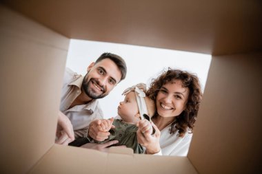 Küçük bir kızı kucağında tutan ve kutunun içine bakan mutlu ebeveynler.