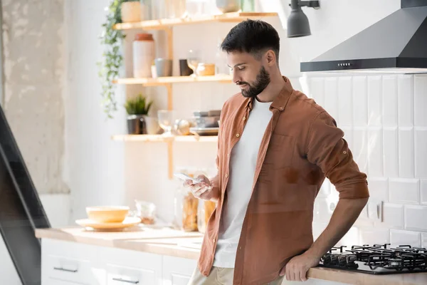 Γενειοφόρος Άνθρωπος Μηνυμάτων Στο Smartphone Ενώ Στέκεται Κοντά Κουζίνα — Φωτογραφία Αρχείου