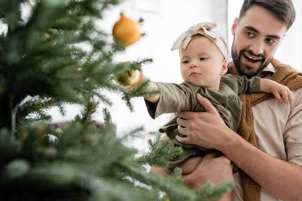 Heyecanlı baba süslemeli Noel ağacının yanında küçük kızını tutuyor.