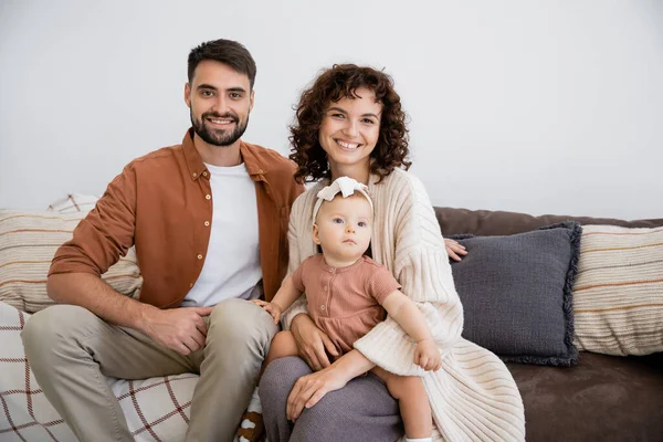 Mãe Alegre Segurando Filha Infantil Perto Marido Sorridente Sentado Sofá — Fotografia de Stock